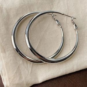 Close-up of polished silver hoop earrings with metallic finish on textured beige fabric