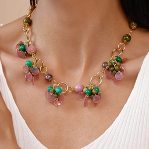 Detail of layered gold necklace featuring green beads and a pink circular shell pendant