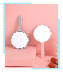 Close-up of pink and grey round handheld mirrors with plastic handles on a vanity table