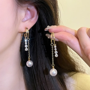 Detail of long gold tassel earrings with zircon stones and a round white pearl on ear
