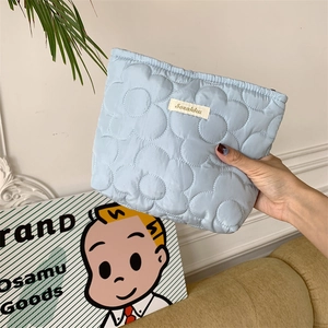 Detail of light blue quilted makeup bag featuring a 3D floral stitch design and soft texture