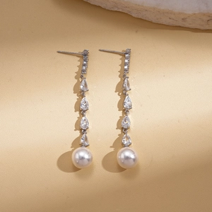 Elegant silver drop earrings with zircons and pearls on a textured stone background