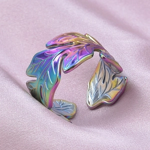 Detailed macro view of an iridescent rainbow steel leaf ring on pink silk fabric background