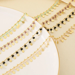 Layered gold necklaces with colorful beads and water drop pendants on white ceramic tray