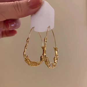 Detail of gold metal earrings with irregular melted texture on white display card