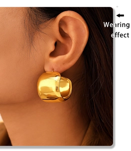 Close-up of a large chunky gold C-shaped hoop earring shown on a model's ear