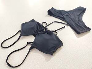 Flat lay of black two-piece bikini set with tie-neck bow and high-cut bottoms detail