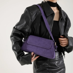 Close-up of a purple suede baguette shoulder bag styled with a black leather outfit