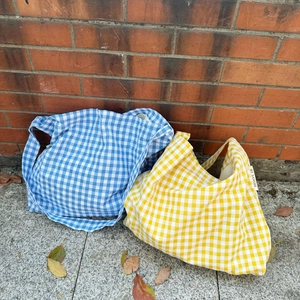 Detail of blue and yellow plaid canvas tote bags against a vintage red brick wall