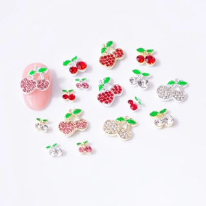 Macro detail of alloy cherry nail charms with rhinestones and green enamel on a fake nail