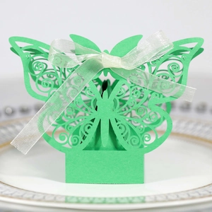 Detail of laser-cut green butterfly wedding favor box with a white ribbon on a plate