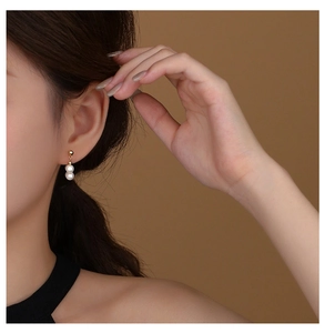 Close-up detail of double white pearls on gold drop earrings worn by a model