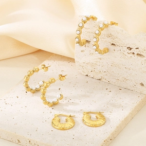 Gros plan de boucles d'oreilles dorées en forme de C avec perles et texture métallique