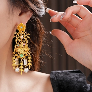 Detalle de pendientes vintage dorados con motivos de aves y flores en una modelo