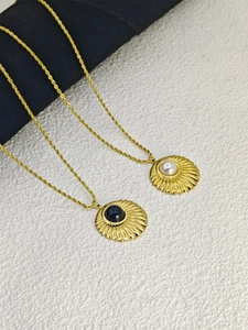 Detailed close-up of gold necklaces featuring shell-textured pendants with pearl and onyx stones