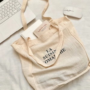 Flat lay of a beige canvas tote bag with black letter print on a minimalist desktop