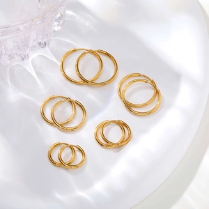 Set of five polished gold hoop earrings in varying sizes on a white textured background