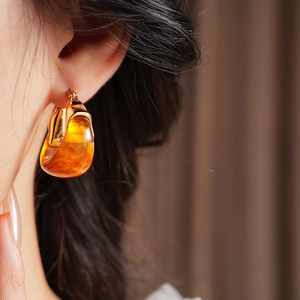 Gros plan sur boucle d'oreille en résine ambre et base dorée sur l'oreille