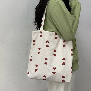 Detail of red heart patterns on cream canvas tote bag worn with a casual green sweatshirt