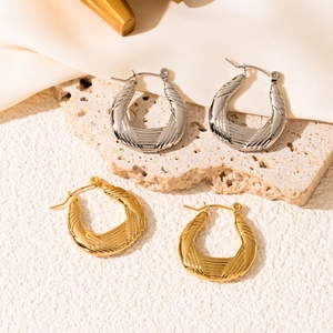 Detailed close-up of textured U-shaped earrings in gold and silver on a beige stone base