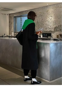 Lifestyle shot of a woman in a black coat wearing a green hooded scarf shawl with gloves