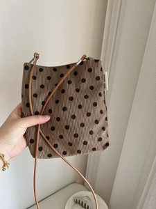 Detail of a brown polka dot corduroy crossbody bag with a white 'simple wish' label