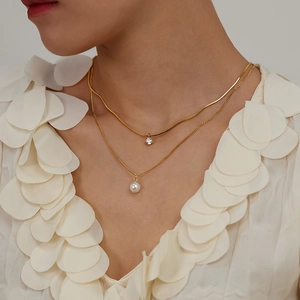 Detail of double-layer gold necklace featuring a pearl pendant and sparkling zircon stone
