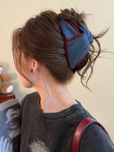 Detail of a large blue denim bow hair claw clip with burgundy trim worn by a model