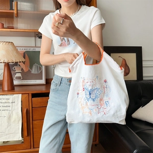 Détail du sac en toile blanche avec broderie papillon bleue et bordure orange vif