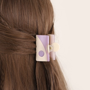 Square claw clip in purple and beige matte acetate holding a brown braided hair bun