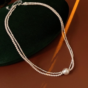 Detail of a layered pearl and silver necklace with a large round pendant on green velvet
