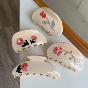 Detailed view of four beige floral claw clips with red roses and rhinestone accents