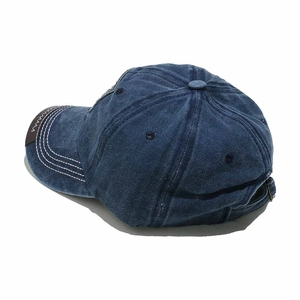 Detail view of navy blue washed denim baseball cap with ventilation holes and metal buckle
