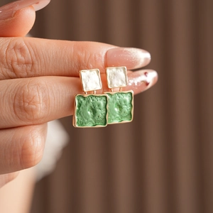 Détail de boucles d'oreilles carrées en émail vert et blanc avec bords dorés sur tissu