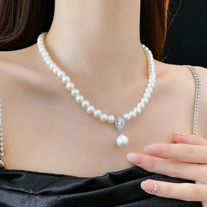 Detail shot of a pearl necklace with a sparkling zircon teardrop pendant on a model