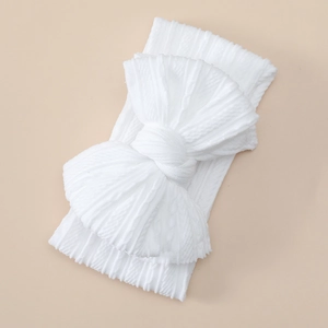 Detail of soft white knitted baby headband with oversized bow and intricate jacquard texture