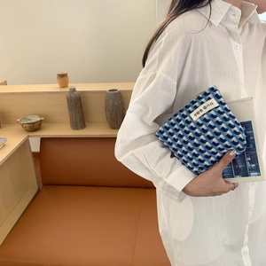 Détail macro d'une pochette tissée à carreaux bleu et blanc tenue par un modèle
