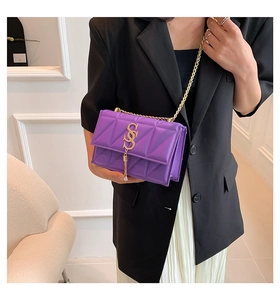 Detail of purple quilted crossbody bag with gold chain strap and S-logo worn by a model