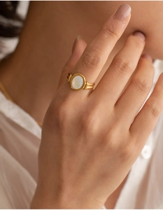 Close-up of golden ring with oval white shell gemstone worn on the finger