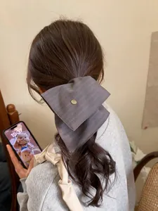Detail of grey striped bow hairband with a gold logo emblem worn on a high ponytail