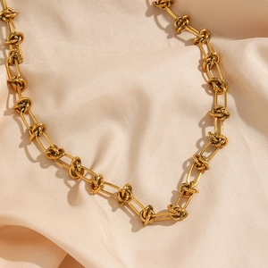 Minimalist golden knot chain necklace featuring unique twisted link design on silk fabric