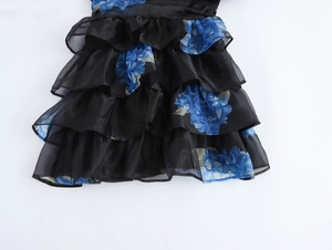 Dettaglio di abito nero in organza con stampa floreale blu e orlo a balze sovrapposte