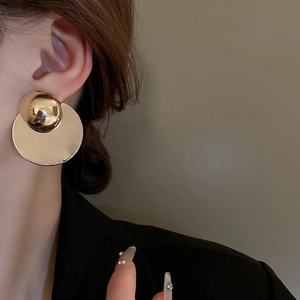 Close-up of a model wearing large golden geometric stud earrings with a mirrored finish