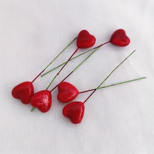 Close-up of six glossy red heart-shaped cake toppers on slim stems over white fabric