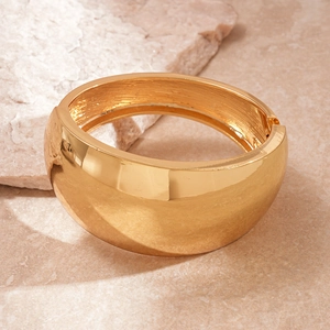 Macro view of wide gold irregular metal cuff bracelet on a natural marble background