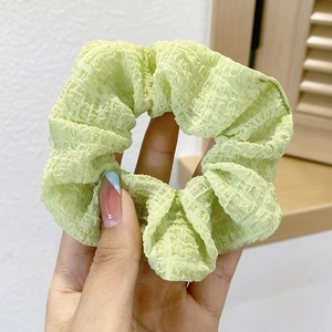 Close-up of a green polka dot scrunchie being held by hand in soft natural light