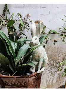 Detail of vintage resin rabbit sculpture with distressed finish among garden greenery