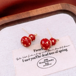 Detailed close-up of 18k gold plated red gourd-shaped stud earrings on a wooden base
