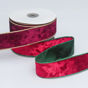 Detail of burgundy velvet ribbon with green back and gold edges on a white spool