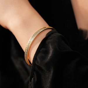 Detail of golden cuff bracelet featuring intricate honeycomb texture on a dark background